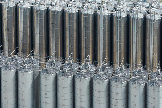 Aerial view of storage facilities for petrochemical products featuring rows of tall stainless steel tanks with industrial piping and ventilation systems in Poland.