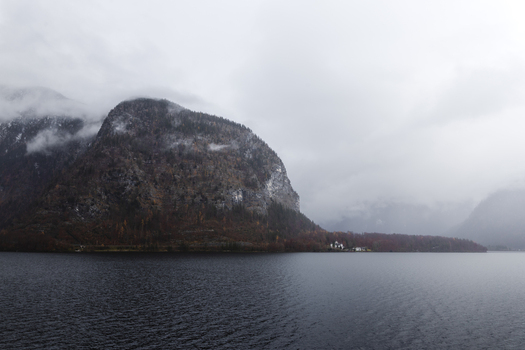 View of steep forested mountains shrouded in thick mist and low clouds overlooking the calm waters of Hallstatter See in Hallstatt Upper Austria Austria. View of steep forested mountains shrouded in thick mist and low clouds overlooking the calm waters of Hallstatter See in Hallstatt Upper Austria Austria.