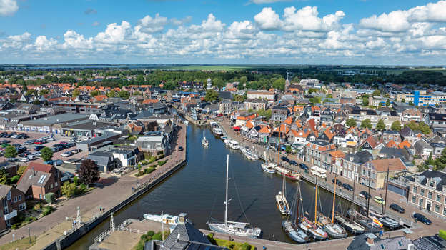 Aerial view of the canal and town center of Lemmer with sailboats moored along the quays surrounded by traditional Dutch rooftops under a blue sky in Lemmer Friesland Netherlands. Aerial view of the canal and town center of Lemmer with sailboats moored along the quays surrounded by traditional Dutch rooftops under a blue sky in Lemmer Friesland Netherlands.