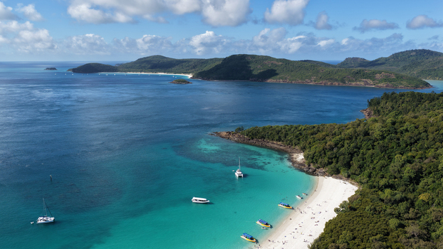 Aerial view of Whitehaven Beach featuring turquoise water white sand lush forest and boats anchored in the bay in Whitsundays Queensland Australia.