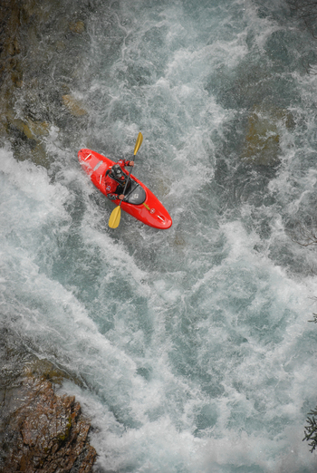View of a person in a red kayak navigating through the white water rapids of the Rio Manso amidst churning turquoise water San Carlos de Bariloche Rio Negro Argentina. View of a person in a red kayak navigating through the white water rapids of the Rio Manso amidst churning turquoise water San Carlos de Bariloche Rio Negro Argentina.