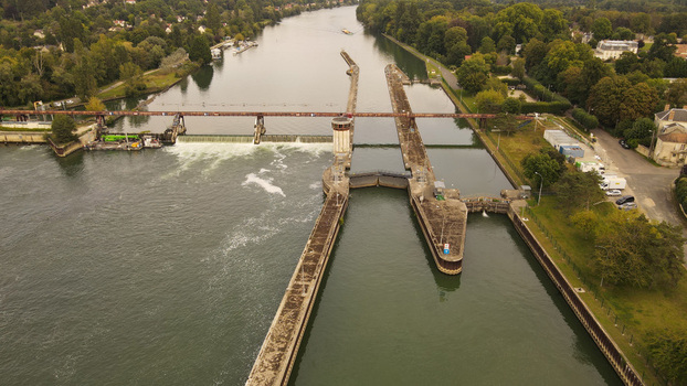 Aerial view of the lock and dam on the Seine River with concrete walls and flowing water surrounded by lush trees in Chartrettes Ile de France France. Aerial view of the lock and dam on the Seine River with concrete walls and flowing water surrounded by lush trees in Chartrettes Ile de France France.