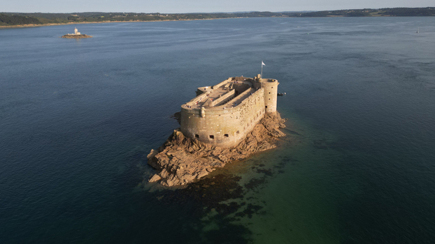 Aerial view of the imposing Ch&acirc;teau du Taureau a stone fortress standing resiliently amidst the dark blue sea contrasted by the clear turquoise shallows Plouezoc h Bretagne France.