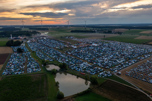 Aerial view of the Open Beatz Festival campsite with thousands of tents and cars near wind turbines under a sunset sky in Herzogenaurach Bayern Germany.