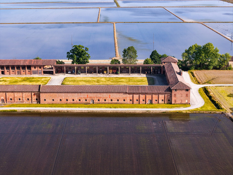 Aerial view of Tenuta Colombara historic farmstead with brick buildings and flooded rice fields in Livorno Ferraris Piemonte Italy.