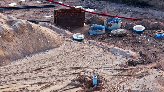 Aerial view of a construction site featuring piles of sand exposed pipes and manhole covers on the ground in Latvia. Aerial view of a construction site featuring piles of sand exposed pipes and manhole covers on the ground in Latvia.