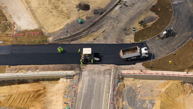 Aerial view of Black Cat Roundabout construction site with heavy machinery asphalt paving and workers in high visibility clothing in Chawston England United Kingdom. Aerial view of Black Cat Roundabout construction site with heavy machinery asphalt paving and workers in high visibility clothing in Chawston England United Kingdom.