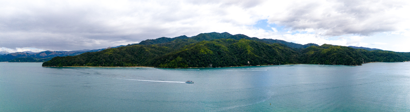 Aerial view of a water taxi cutting through the teal waters towards the lush green mountainous coastline Abel Tasman National Park Tasman Region New Zealand. Aerial view of a water taxi cutting through the teal waters towards the lush green mountainous coastline Abel Tasman National Park Tasman Region New Zealand.
