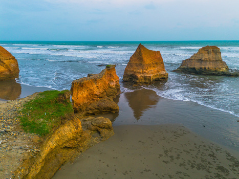 Aerial view of orange rock formations on a sandy beach with turquoise ocean waves and green cliffs in Bali Bali Indonesia. Aerial view of orange rock formations on a sandy beach with turquoise ocean waves and green cliffs in Bali Bali Indonesia.