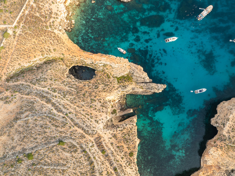 Aerial view of turquoise waters meet the rugged sun baked cliffs creating a stunning contrast of blues and earthy tones at the Blue Lagoon Comino Malta. Aerial view of turquoise waters meet the rugged sun baked cliffs creating a stunning contrast of blues and earthy tones at the Blue Lagoon Comino Malta.
