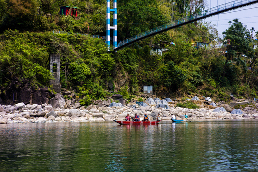 Meghalaya India 31 March 2023 View of people in small boats on a river with a suspension bridge above and a rocky bank with tents in the background. Meghalaya India 31 March 2023 View of people in small boats on a river with a suspension bridge above and a rocky bank with tents in the background.