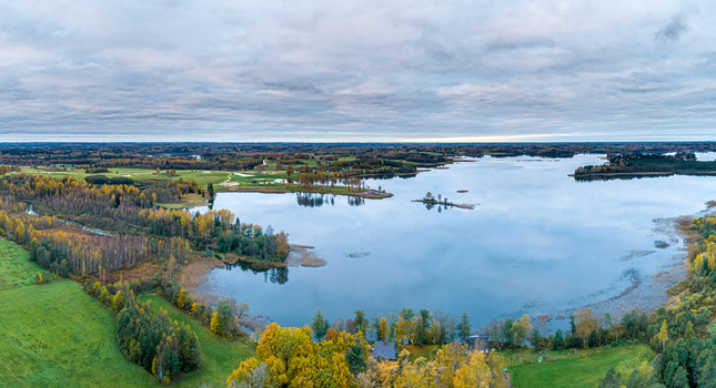 Aerial view of the autumn landscape surrounding the lake in Cesis featuring vibrant foliage calm water and green meadows under a cloudy sky in Cesis Cesis Municipality Latvia. Aerial view of the autumn landscape surrounding the lake in Cesis featuring vibrant foliage calm water and green meadows under a cloudy sky in Cesis Cesis Municipality Latvia.