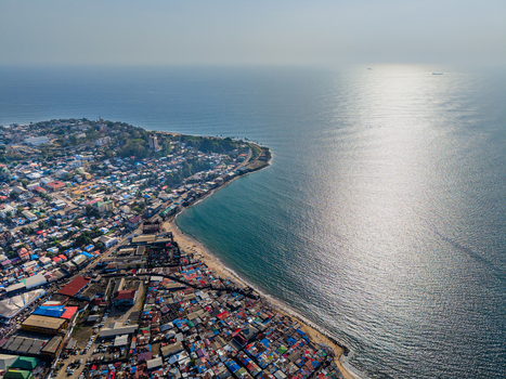 Aerial view of dense urban sprawl along the coastline with colorful rooftops and the sun reflecting on the Atlantic Ocean Monrovia Montserrado Liberia. Aerial view of dense urban sprawl along the coastline with colorful rooftops and the sun reflecting on the Atlantic Ocean Monrovia Montserrado Liberia.