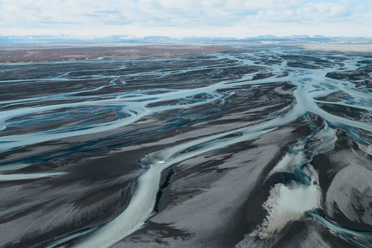 Aerial view of a braided glacial river system with light blue water flowing through dark volcanic sand plains in Skaftarhreppur Iceland.