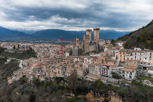 Aerial view of the medieval village of Pacentro featuring the historic Caldora Castle towers and stone houses against snow capped mountains in Pacentro Abruzzo Italy. Aerial view of the medieval village of Pacentro featuring the historic Caldora Castle towers and stone houses against snow capped mountains in Pacentro Abruzzo Italy.