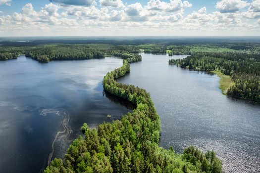 Aerial view of the narrow forested ridge of Liesjarvi National Park separating the dark blue waters of the lake under a bright sky in Tammela Finland. Aerial view of the narrow forested ridge of Liesjarvi National Park separating the dark blue waters of the lake under a bright sky in Tammela Finland.