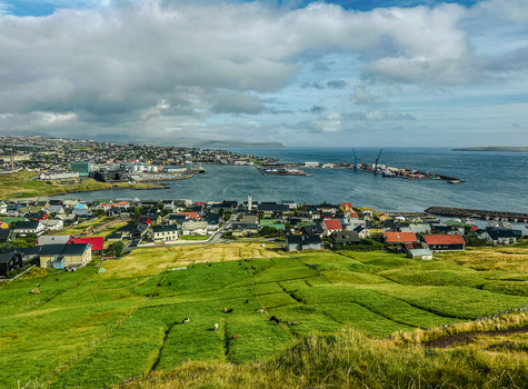 View of the colorful houses and harbor of Torshavn nestled among green hills under a cloudy sky in the Faroe Islands. View of the colorful houses and harbor of Torshavn nestled among green hills under a cloudy sky in the Faroe Islands.