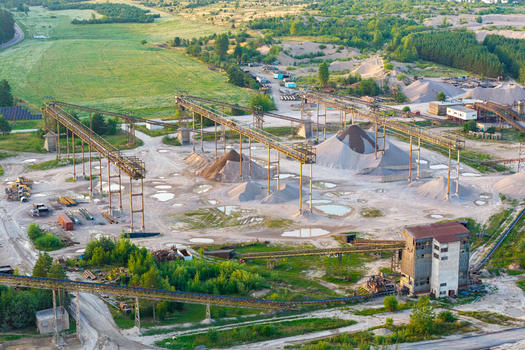 Aerial view of a large scale sand and gravel mine with conveyor belts piles of extracted material industrial buildings and surrounding green forest in Poland.