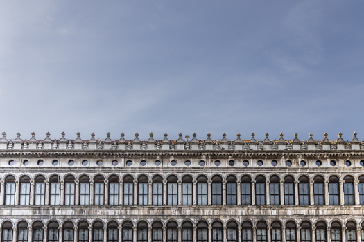 View of the historic Procuratie Nuove building with its repetitive arched windows and ornate facade under a clear blue sky in Venice Veneto Italy. View of the historic Procuratie Nuove building with its repetitive arched windows and ornate facade under a clear blue sky in Venice Veneto Italy.