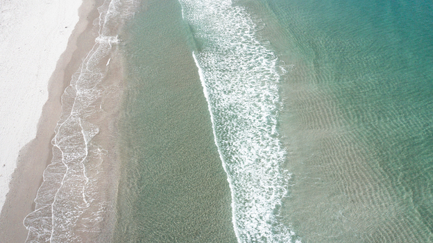 Aerial view of the pristine white sand and turquoise waters of Omaha Beach in Omaha Auckland New Zealand.