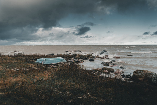 View of a blue boat resting on the rocky grassy shore of Vormsi island under a dramatic stormy sky in Laane County Estonia.
