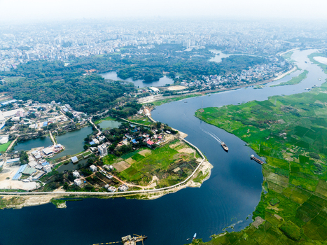 Aerial view of a winding river flowing through lush green fields and rural settlements with the dense urban skyline of Dhaka in the background Dhaka Dhaka Division Bangladesh. Aerial view of a winding river flowing through lush green fields and rural settlements with the dense urban skyline of Dhaka in the background Dhaka Dhaka Division Bangladesh.