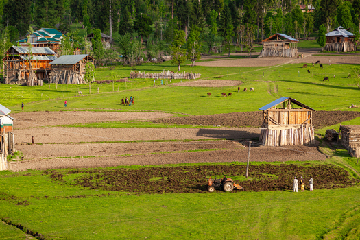 View of traditional wooden houses and agricultural fields with a tractor plowing the land and people standing nearby in Arang Kel Azad Kashmir Pakistan. View of traditional wooden houses and agricultural fields with a tractor plowing the land and people standing nearby in Arang Kel Azad Kashmir Pakistan.