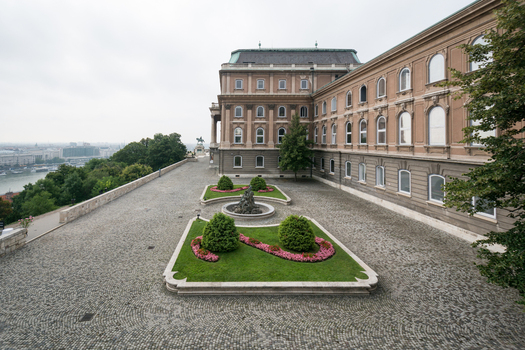 View of the historic Buda Castle with its elegant architecture cobblestone courtyard and manicured garden beds overlooking the Danube river in Budapest Hungary.