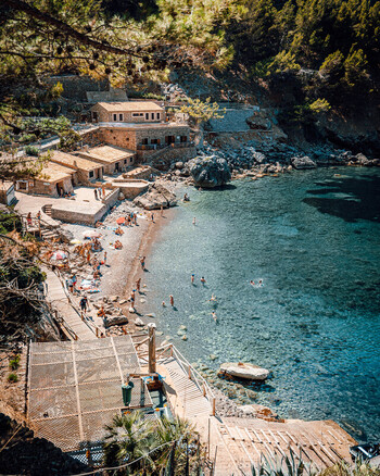 Cala Deia Spain 15 September 2023 View of the rocky cove and turquoise waters of Cala Deia with stone buildings sunbathers on the pebble beach and lush pine trees. Cala Deia Spain 15 September 2023 View of the rocky cove and turquoise waters of Cala Deia with stone buildings sunbathers on the pebble beach and lush pine trees.