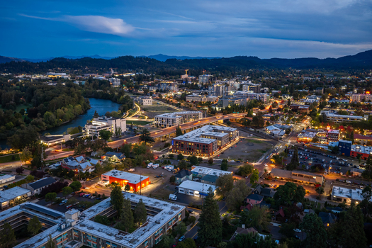Aerial view of Eugene at twilight featuring the Willamette River illuminated buildings and roads with light trails winding through the landscape in Eugene Oregon United States. Aerial view of Eugene at twilight featuring the Willamette River illuminated buildings and roads with light trails winding through the landscape in Eugene Oregon United States.