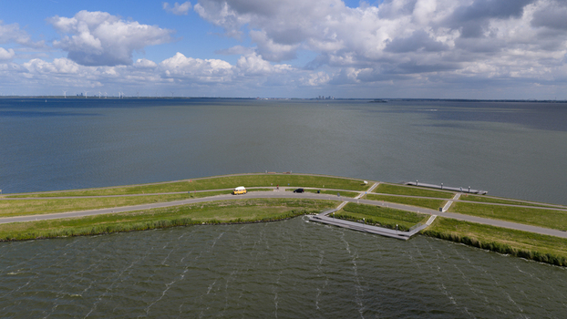 Aerial view of a grassy dike separating water bodies with a yellow van parked on the road in Uitdam North Holland Netherlands.