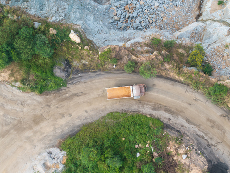 Aerial view of a dump truck driving on a dirt road through a mining site with rocky terrain and surrounding greenery in Bukit Tambun Penang Malaysia. Aerial view of a dump truck driving on a dirt road through a mining site with rocky terrain and surrounding greenery in Bukit Tambun Penang Malaysia.
