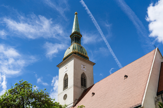 View of the historic St. Martin s Cathedral spire and tower under a bright blue sky with wispy clouds and a contrail Bratislava Bratislava Region Slovakia. View of the historic St. Martin s Cathedral spire and tower under a bright blue sky with wispy clouds and a contrail Bratislava Bratislava Region Slovakia.