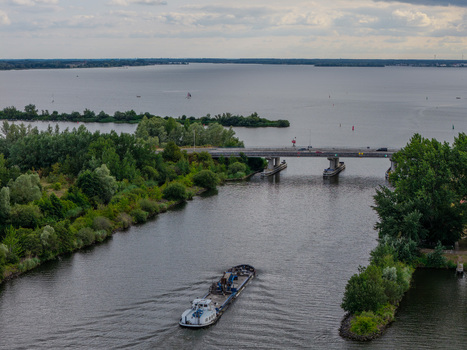 Aerial view of Harderhaven with a cargo barge navigating the canal towards the bridge surrounded by lush green trees and the expansive waters in Zeewolde Flevoland Netherlands.