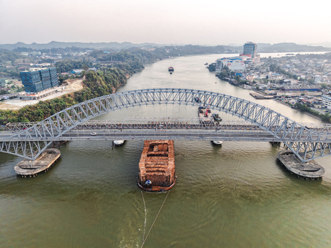 Aerial view of Jembatan Mahakam I crossing the Mahakam River with a barge carrying logs passing underneath near urban areas in Kecamatan Samarinda Seberang Kalimantan Timur Indonesia. Aerial view of Jembatan Mahakam I crossing the Mahakam River with a barge carrying logs passing underneath near urban areas in Kecamatan Samarinda Seberang Kalimantan Timur Indonesia.