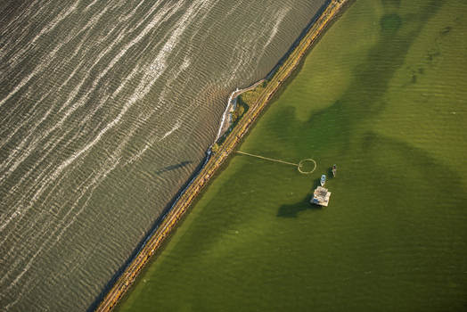 Aerial view of a coastal barrier separating a dark sea from a calm green lagoon featuring a small stilt house and two small boats in Rio de Janeiro Rio de Janeiro Brazil. Aerial view of a coastal barrier separating a dark sea from a calm green lagoon featuring a small stilt house and two small boats in Rio de Janeiro Rio de Janeiro Brazil.