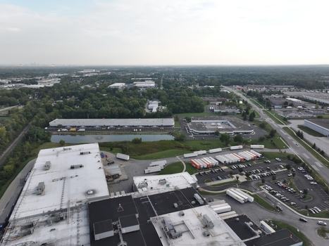 Aerial view of a large industrial logistics facility with warehouses loading docks parked semi trucks and a small pond surrounded by trees in Indianapolis Indiana United States. Aerial view of a large industrial logistics facility with warehouses loading docks parked semi trucks and a small pond surrounded by trees in Indianapolis Indiana United States.