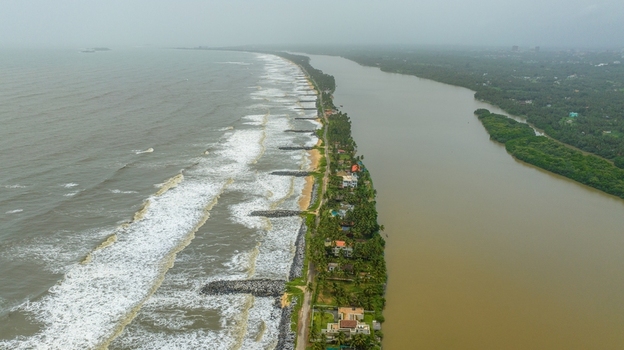 Aerial view of Mattu Beach showing the narrow land strip between the Arabian Sea and backwaters with coastal vegetation breakwaters and houses in Udupi Karnataka India.