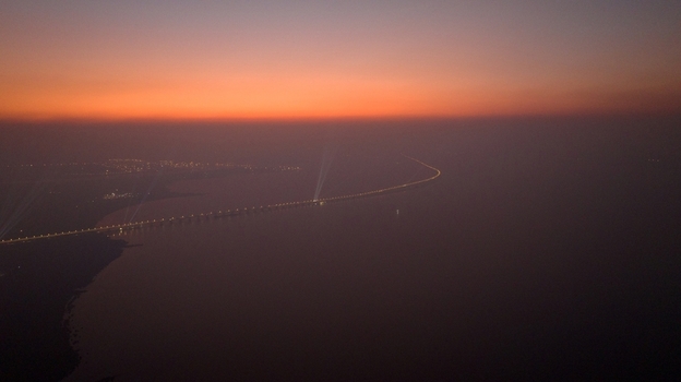 Aerial view of a long bridge illuminated at dusk stretching across the calm water with city lights glowing in the distance in Nagda Madhya Pradesh India. Aerial view of a long bridge illuminated at dusk stretching across the calm water with city lights glowing in the distance in Nagda Madhya Pradesh India.