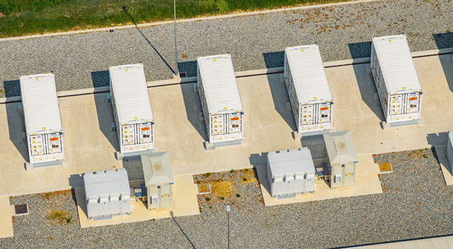 Aerial view of utility scale battery storage containers and electrical equipment installed next to a large photovoltaic solar farm in Italy.