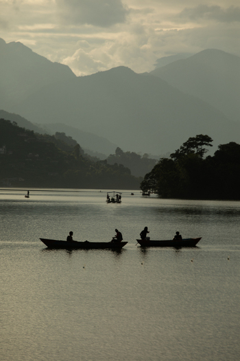 Pokhara Nepal 31 July 2026 View of people rowing wooden boats on Phewa Lake with the Himalayan mountains in the background under a cloudy sky.