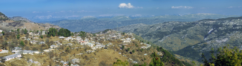 Aerial view of the panoramic landscape of Galiyat featuring scattered houses on rolling hills and distant mountain ranges under a clear blue sky in Galiyat Pakistan.