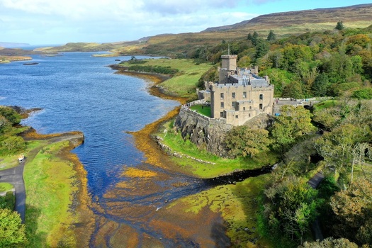 Aerial view of Dunvegan Castle and Gardens situated on a rocky outcrop overlooking the sea with lush green trees and rugged hills in Isle of Skye Scotland United Kingdom. Aerial view of Dunvegan Castle and Gardens situated on a rocky outcrop overlooking the sea with lush green trees and rugged hills in Isle of Skye Scotland United Kingdom.
