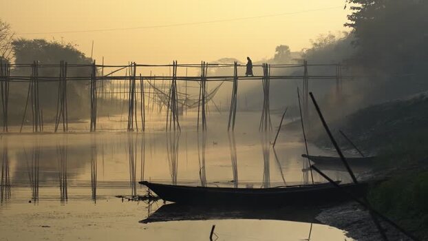 View of a person walking on a bamboo bridge at sunrise Bangladesh.