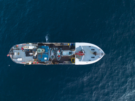 Aerial view of a fishing vessel with deck equipment and inflatable boats navigating the deep blue waters near the remote Sule Stack in Scotland United Kingdom. Aerial view of a fishing vessel with deck equipment and inflatable boats navigating the deep blue waters near the remote Sule Stack in Scotland United Kingdom.