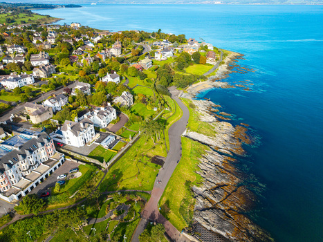 Aerial view of Bangor Harbour and Town featuring historic buildings lush green parks and a coastal path along the rocky shoreline in Bangor Northern Ireland United Kingdom.