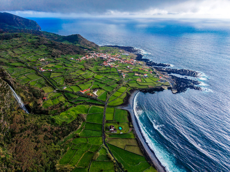Aerial view of verdant fields meet the rugged coastline where ocean waves crash against the volcanic rocks Faj&atilde; Grande Azores Portugal.