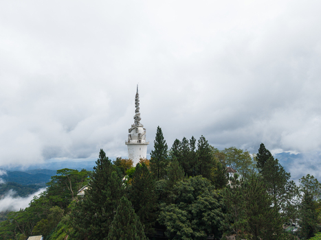 Aerial view of Ambuluwawa Tower rising above lush green forests and misty mountains under a cloudy sky in Gampola Central Province Sri Lanka. Aerial view of Ambuluwawa Tower rising above lush green forests and misty mountains under a cloudy sky in Gampola Central Province Sri Lanka.