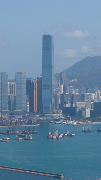 Aerial view of the International Commerce Centre skyscraper rising above Victoria Harbour with cargo barges and mountains under a clear sky Hong Kong Hong Kong. Aerial view of the International Commerce Centre skyscraper rising above Victoria Harbour with cargo barges and mountains under a clear sky Hong Kong Hong Kong.