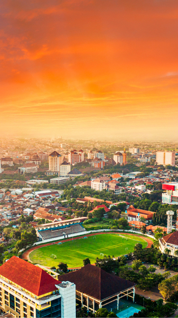 Aerial view of Cakrawala Stadium surrounded by urban buildings and lush greenery under a vibrant sunset sky in Kecamatan Lowokwaru Jawa Timur Indonesia. Aerial view of Cakrawala Stadium surrounded by urban buildings and lush greenery under a vibrant sunset sky in Kecamatan Lowokwaru Jawa Timur Indonesia.